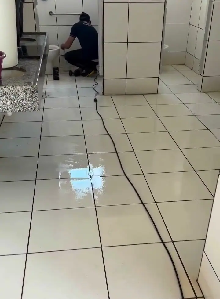 Banheiro coletivo limpo depois da obra, com o profissional terminando os detalhes